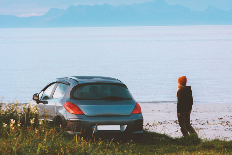 Een vrouw staat naast haar auto aan een meer in Scandinavië